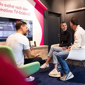Drei Personen im Wohnzimmer testen Smart-TV und Streaming auf dem Fernseher.