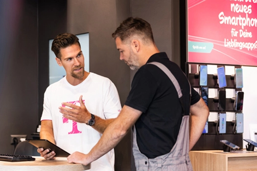 Verkäufer berät Kunden im Handyshop zu Smartphones und Mobilfunkvertrag